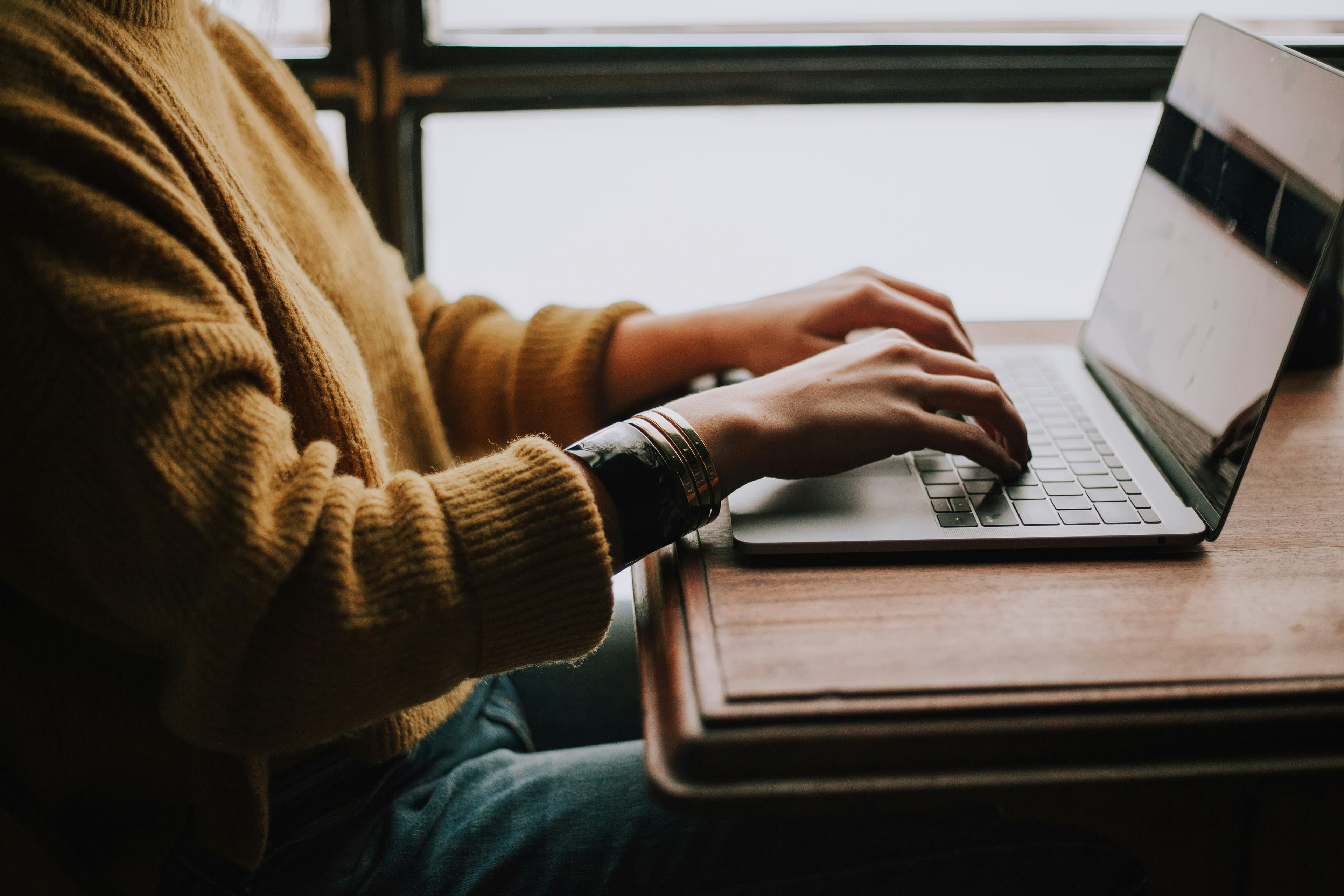 A person typing on a laptop at a wooden desk